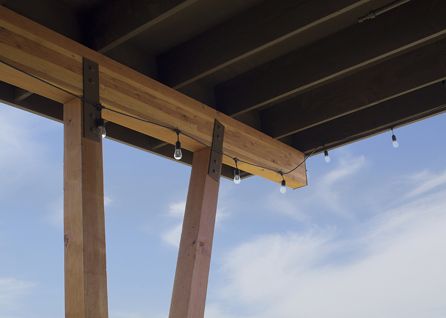 Edison bulbs hang from nail laminated beams used to construct the open-air pavilion